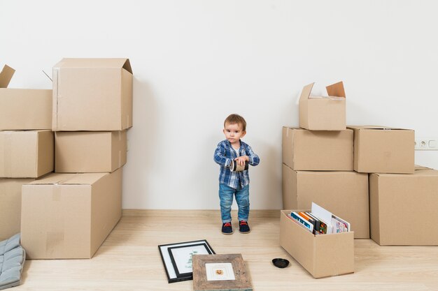 Little baby boy standing between the moving cardboard boxes at new home