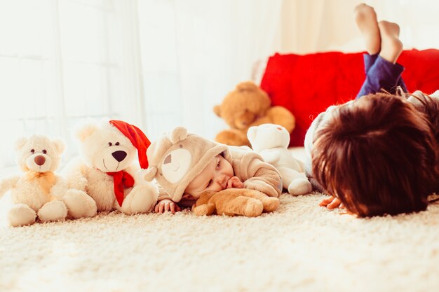 Little baby dressed like a bear lies on fluffy carpet with its m