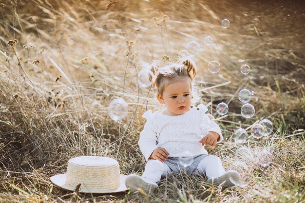 Little baby girl blowing soap bubbles in field