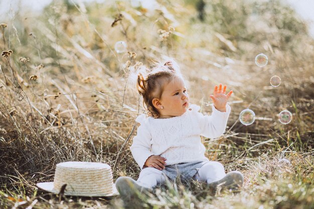 Little baby girl blowing soap bubbles in field