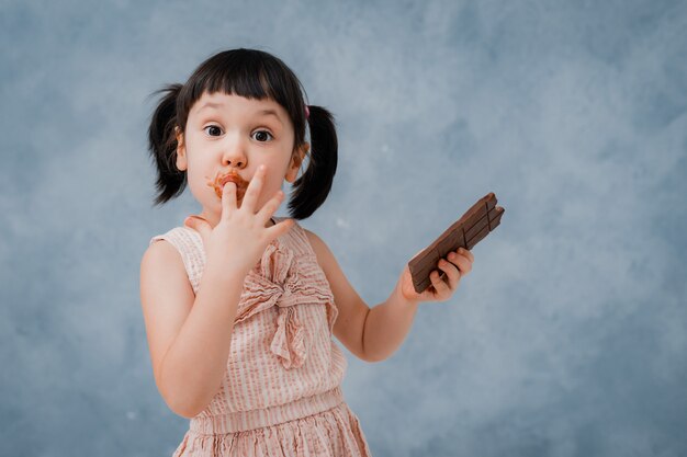 小さな女の赤ちゃんはチョコレートを食べ 彼女の指をなめる プレミアム写真