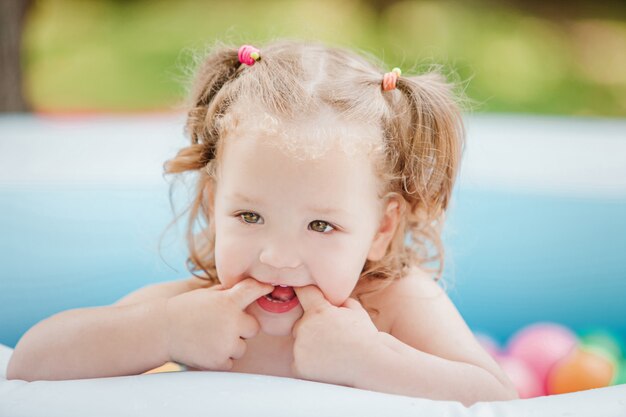 Маленькая девочка играет с игрушками в надувном бассейне в солнечный летний день
