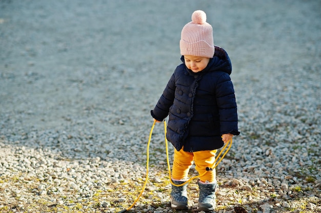 Little baby girl in the sun hold rope jump