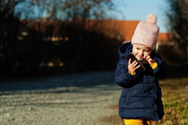 Маленькая девочка в солнечный день держит мобильный телефон в руках