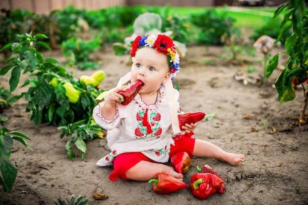 Little baby-girl with a large red pepper sits on the back-yard