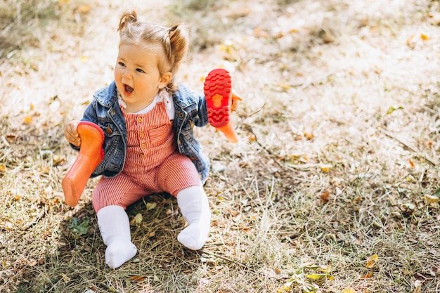 Little baby girl with rain boots sitting in park