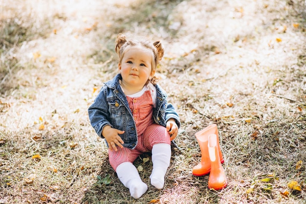 Little baby girl with rain boots sitting in park