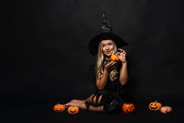 Little barefoot witch showing jack-o-lantern