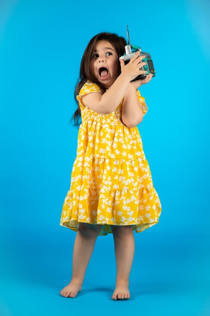 Маленькая красивая улыбающаяся девочка со смешным лицом в полосатом желтом платье позирует на синем фоне в студии
