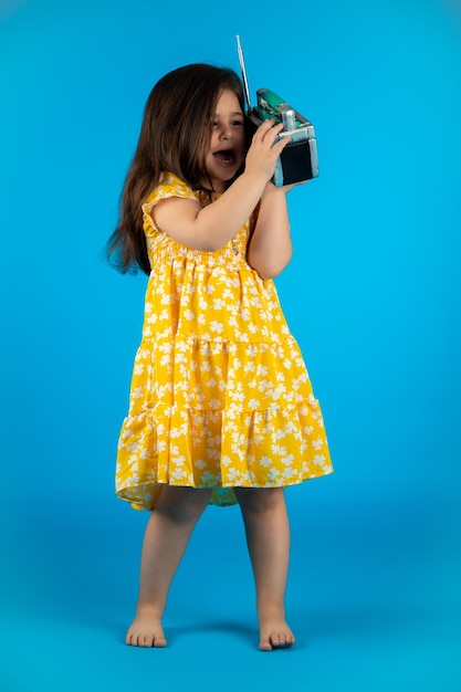 Маленькая красивая улыбающаяся девочка со смешным лицом в полосатом желтом платье позирует на синем фоне в студии