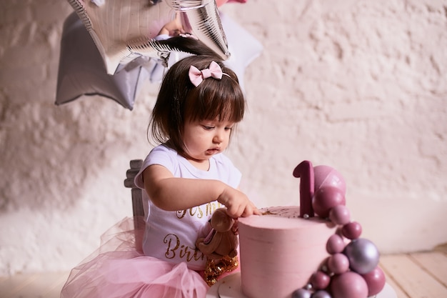 Little birthday girl. Charming baby in pink dress sits on the chair 