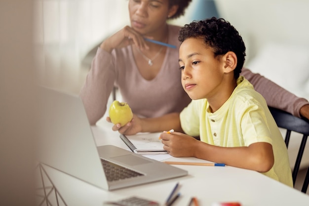 Free photo little black boy using laptop while homeschooling with his mother