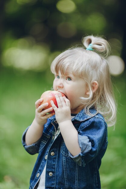 Little blond girl biting an apple