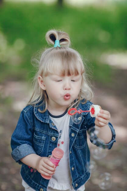 Little blond girl blowing by a pompous and making bubbles