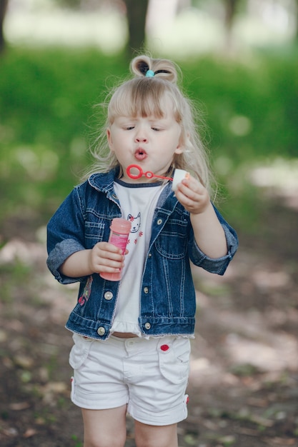 Little blond girl blowing by a pompous and making bubbles