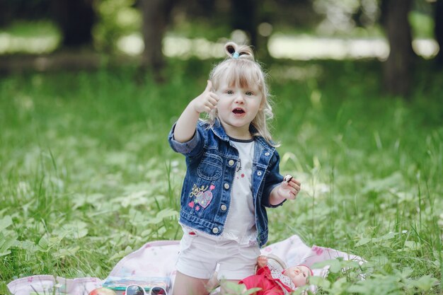 Little blond girl sitting on a picnic blanket with a thumbs up