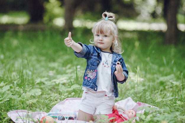 Little blond girl sitting on a picnic blanket with a thumbs up