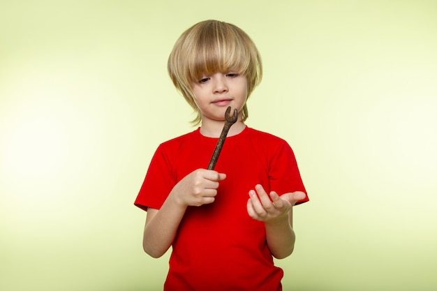 Free photo little blonde boy in red t-shirt and metallic tool on white