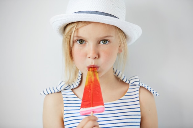 Bambina bionda che indossa cappello bianco e mangia il gelato