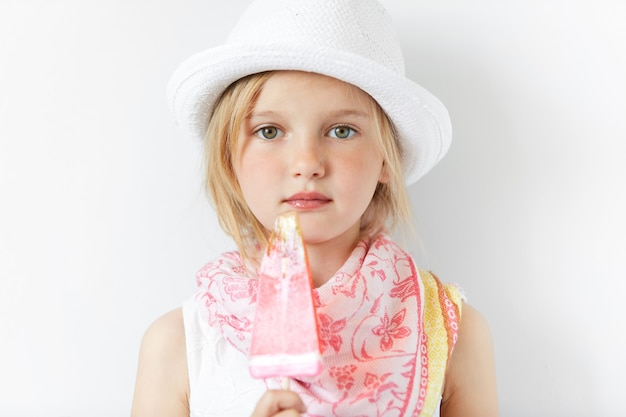 Little blonde girl wearing white hat and eating ice cream