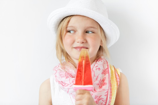 Bambina bionda che indossa cappello bianco e mangia il gelato