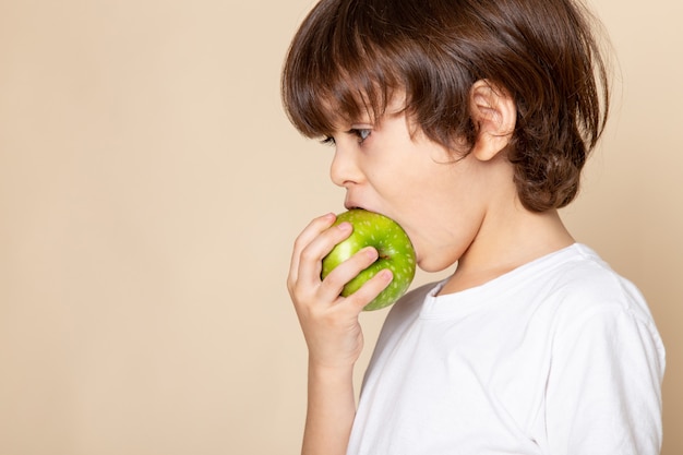 Free photo little boy adorable eating green apple on pink desk