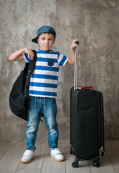 待合室でコンクリートの壁にスーツケースを持って一人で小さな男の子。 Premium写真