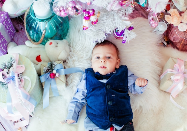 Little boy in blue suit lies among pink toys on the floor 