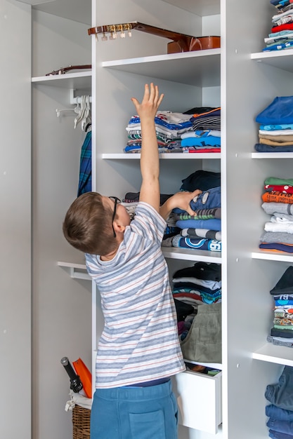 A little boy can't get his guitar off the top shelf of the cabinet.
