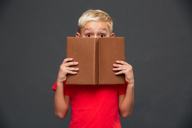 Little boy child covering face with book.