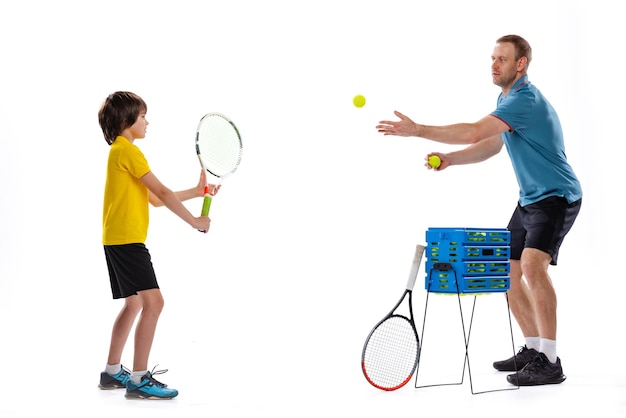 Маленький мальчик учится играть в теннис с профессиональным спортивным инструктором, изолированным на белом фоне студии