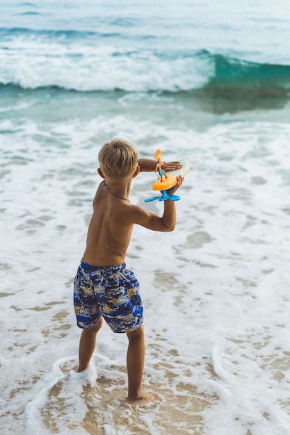 Foto gratuita ragazzino che gioca sulla spiaggia in riva all'oceano.