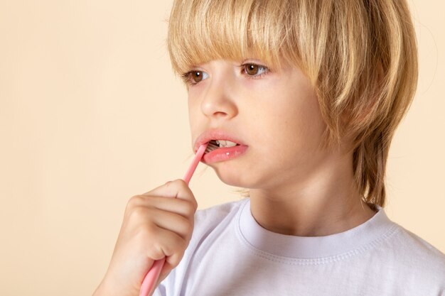 little boy cleaning his teeth blonde in white t-shirt