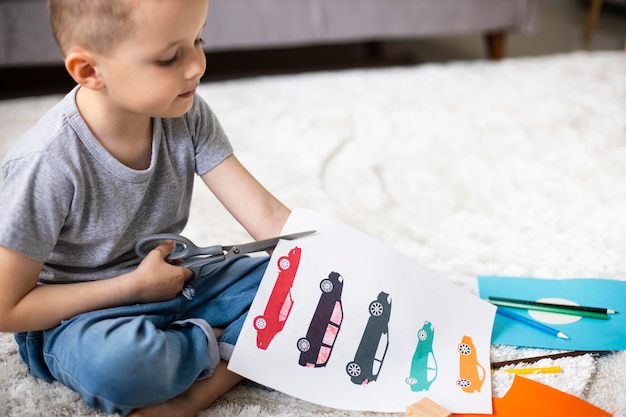 Little boy cutting a paper with car drawings