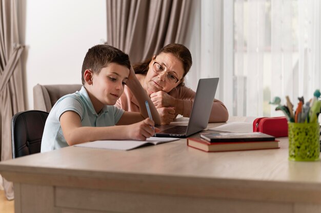 Little boy doing homework with his grandmother on laptop