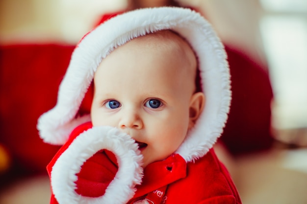 маленький мальчик, одетый, как Санта-Клаус, сидящий в рождественской студии