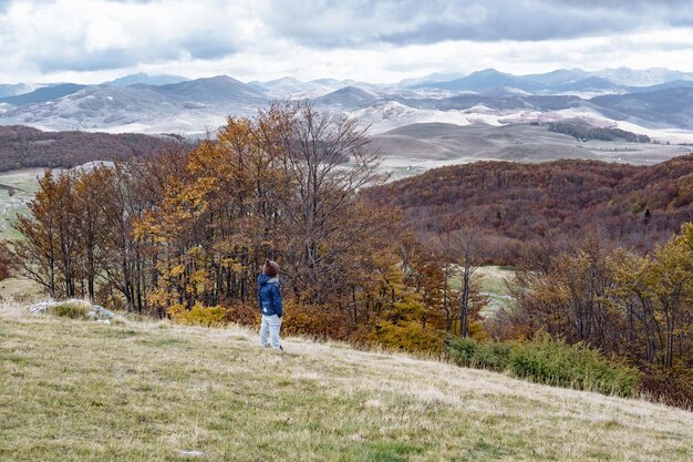 Маленький мальчик в смешной шляпе смотрит на горы Дурмитор Черногория