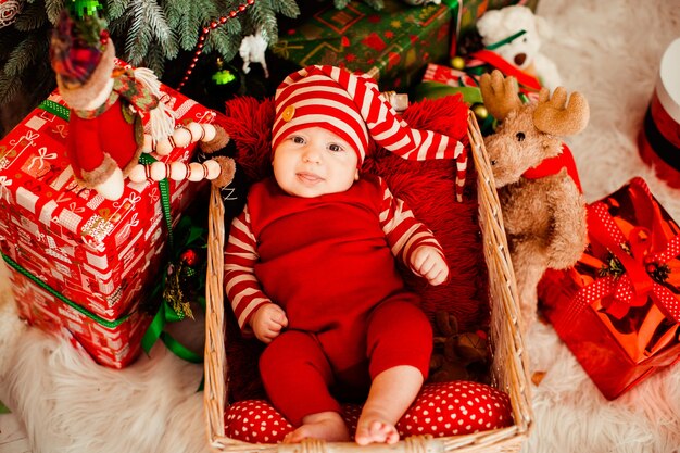 재미 있은 빨간 양복과 긴 모자에 어린 소년 크리스마스 트리 전에 바구니에 놓여