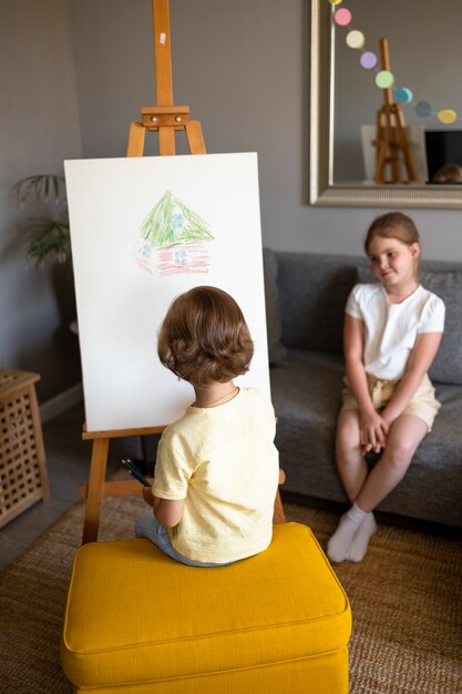 家でイーゼルを使って一緒に描く小さな男の子と女の子