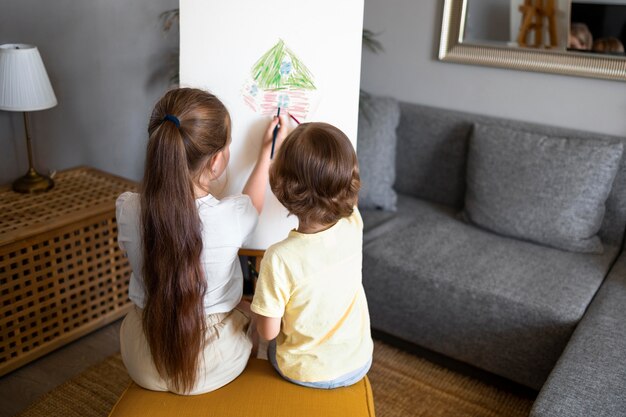 어린 소년과 소녀가 함께 집에서 이젤을 사용하여 그리기