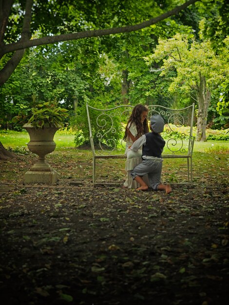 Маленький мальчик на коленях перед маленькой девочкой в саду в окружении зелени