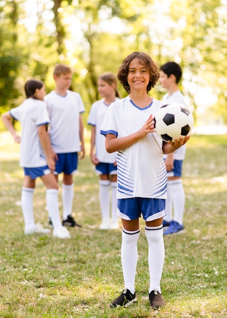 他の子供たちの横にある外のサッカーを保持している小さな男の子