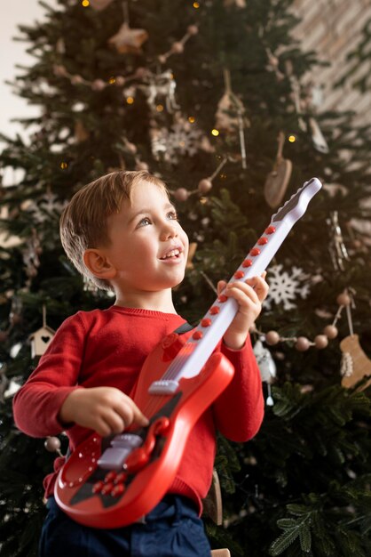 Little boy holding a guitar next to tree
