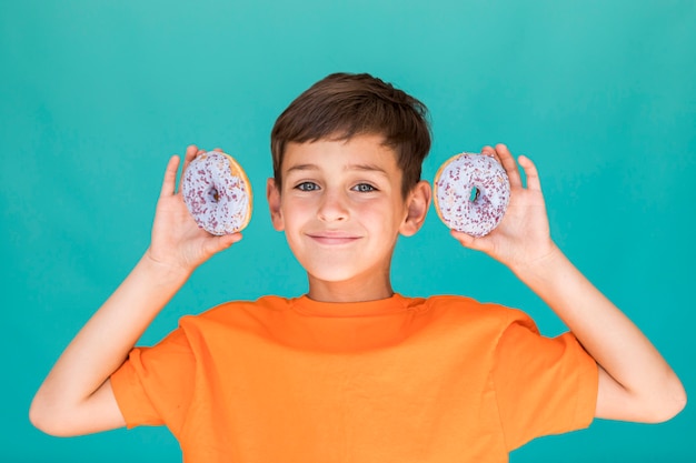 Little boy holding up two glazed doughnuts 