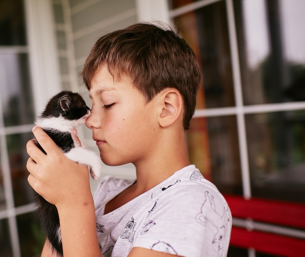 Little boy holds black and white kitty on his shoulder 