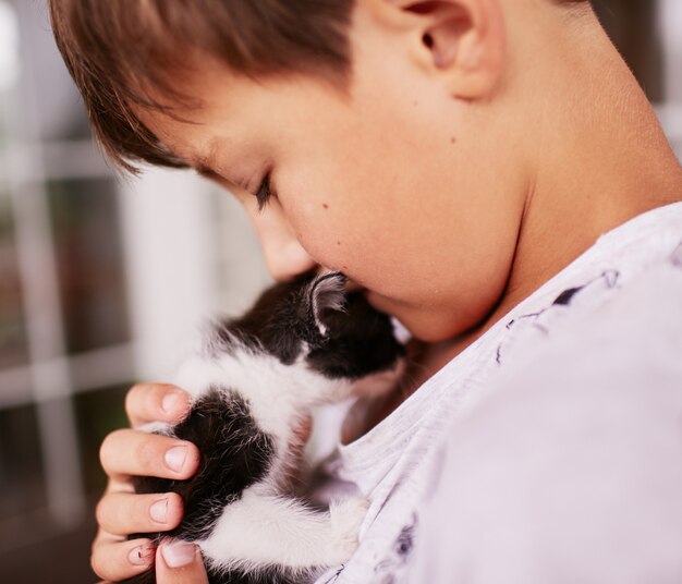 Little boy holds black and white kitty on his shoulder 