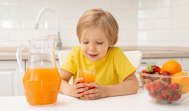 自宅で小さな男の子が果物を食べてジュースを飲む