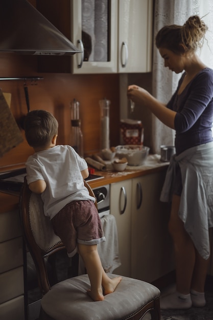 無料写真 キッチンの小さな男の子は、お母さんが料理するのに役立ちます。子供は料理に関わっています。