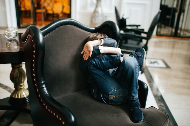Little boy in jeans sits in soft armchair