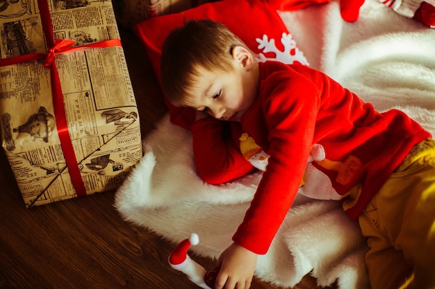 Little boy lies on a white carpet before a Christmas tree 